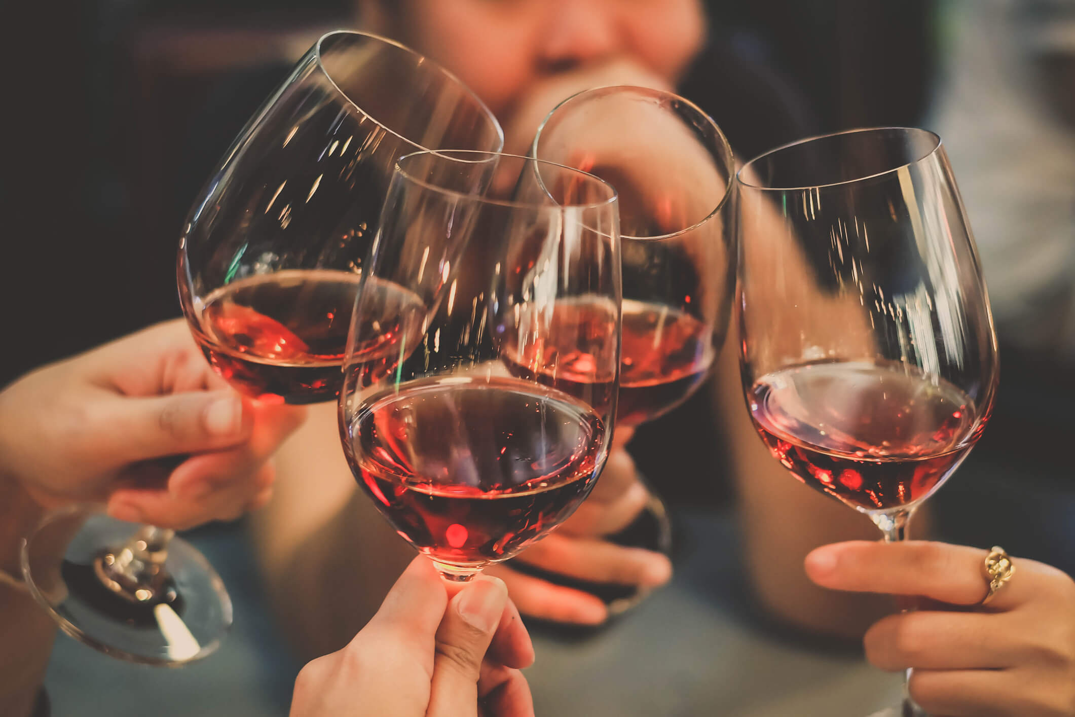 A group of friends clinks wine glasses together, close up.
